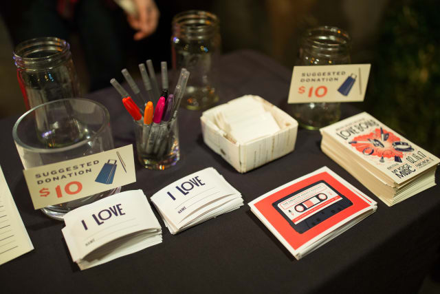 Table display at Love Bomb 2017 event featuring suggested donation signs, colorful pens, and promotional materials for My Voice Music's music education program.